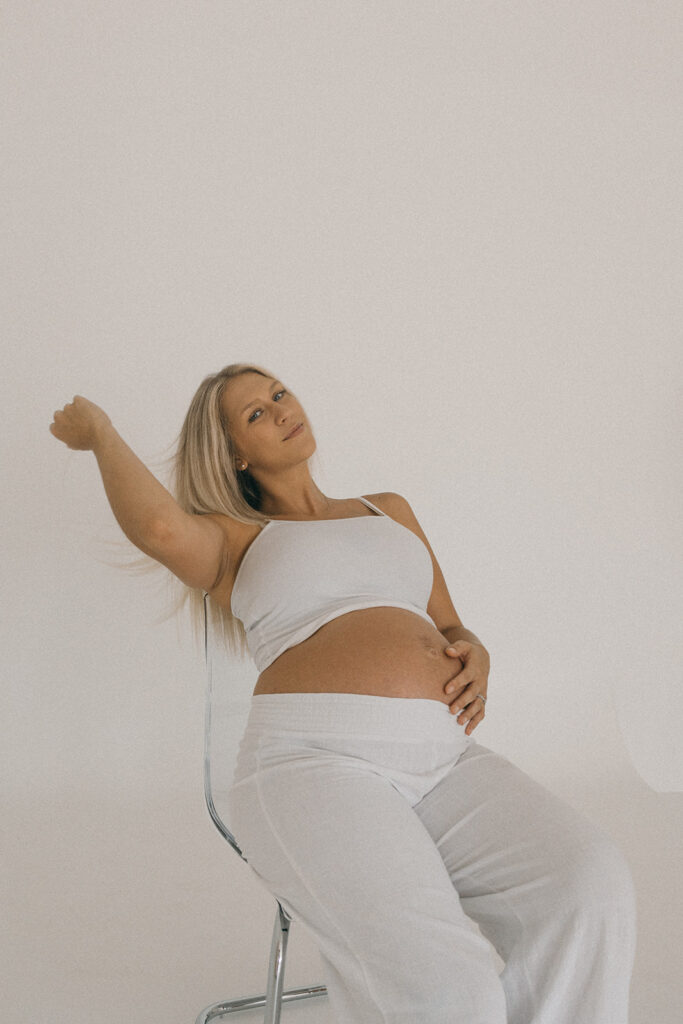 Jacksonville pregnant mom sitting in a chair, running her hands through her hair for a maternity photo session.