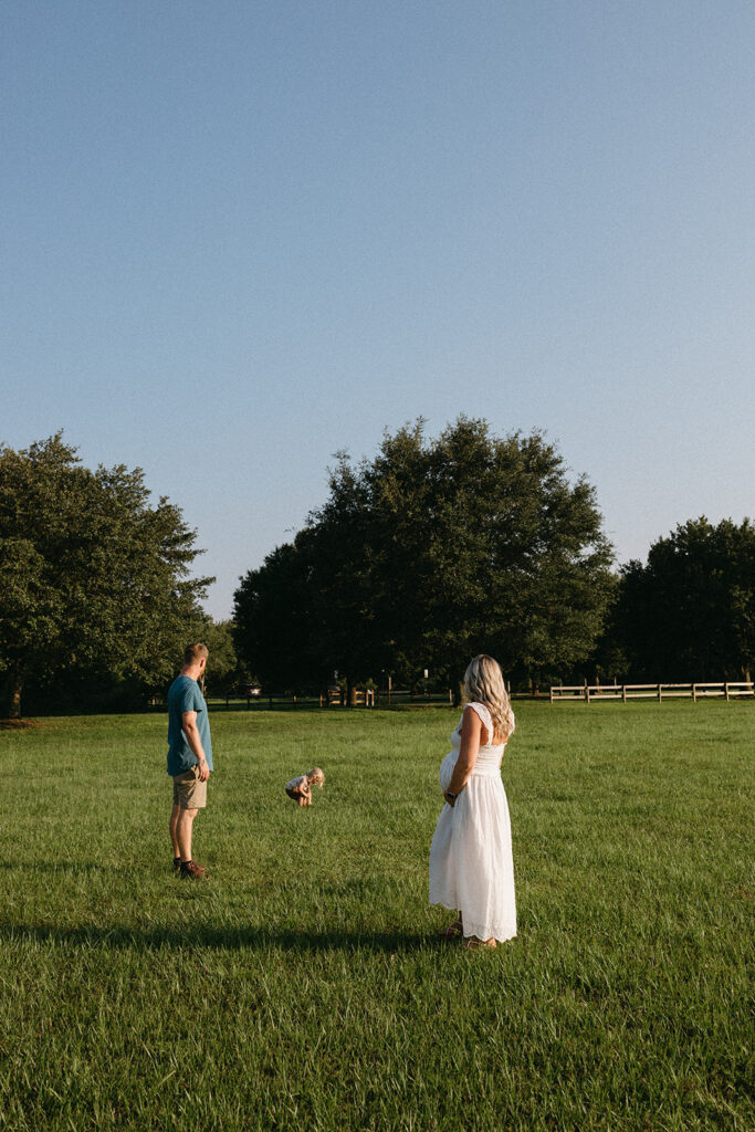 Jacksonville maternity couple watching their son play in the grass. Mother is holding her belly. 