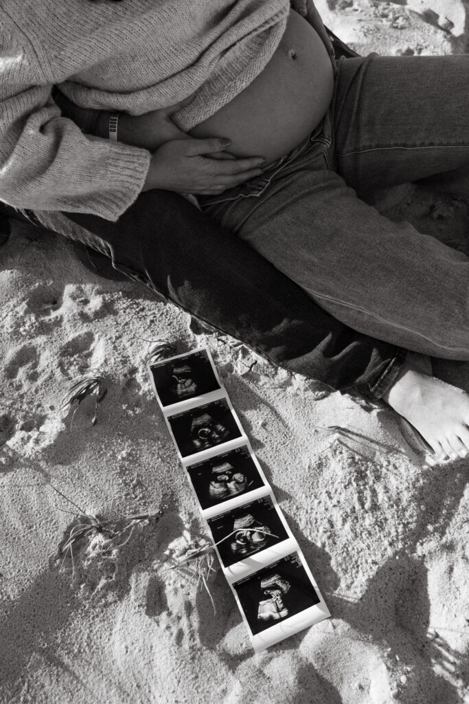 Pregnancy announcement photos in Jacksonville, Fl. Photo of an ultrasound picture sitting on the sand, next to expectant mother's belly