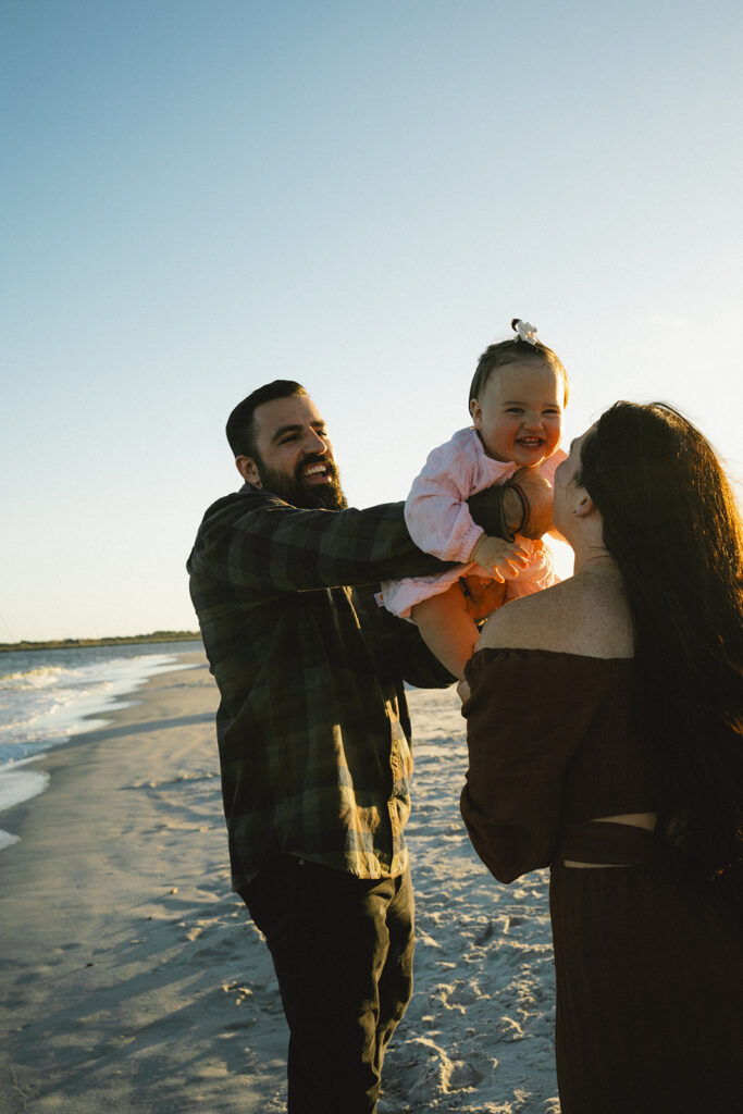 dad holding baby handing her to her mom on a jacksonville beach