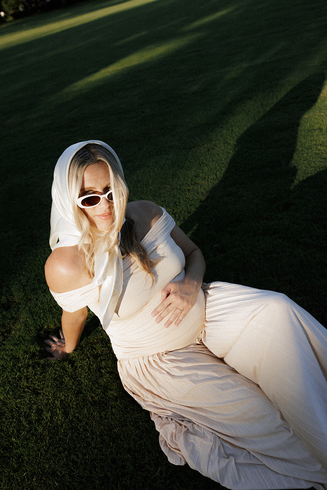 pregnant woman sitting on the grass looking at the camera.