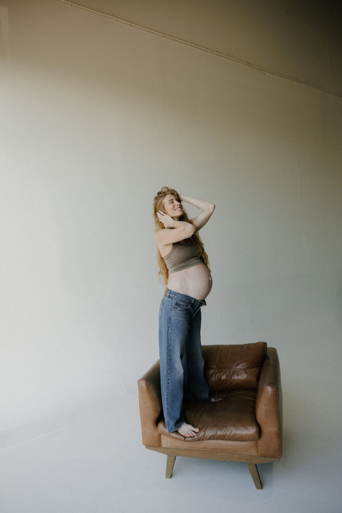 pregnant mom standing on a chair in a jacksonville studio smiling 