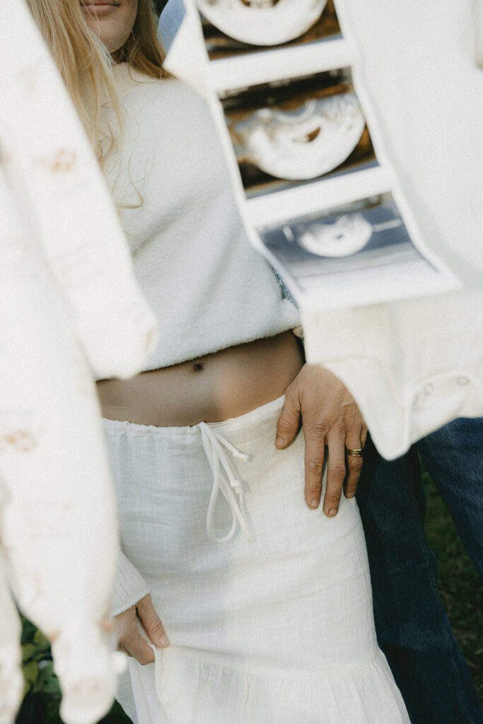 A picture of a moms belly surrounded by baby clothes on a clothesline, including an ultrasound picture in Jacksonville beach fl for pregnancy announcement photos
