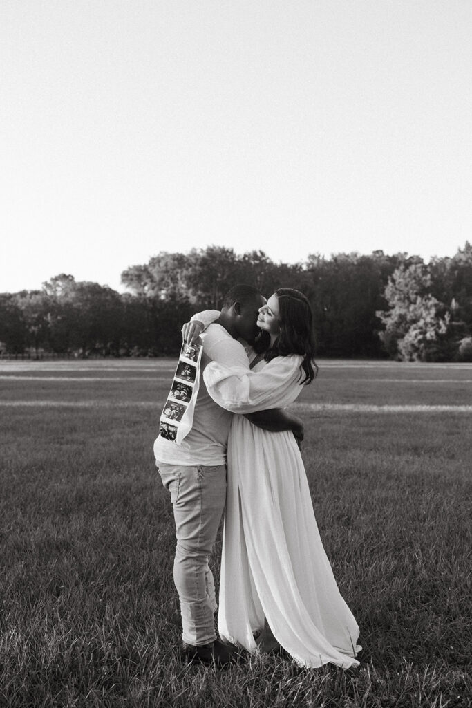 expecting couple hugging while the wife holds an ultrasound picture to announce their pregnancy in Jacksonville, Fl
