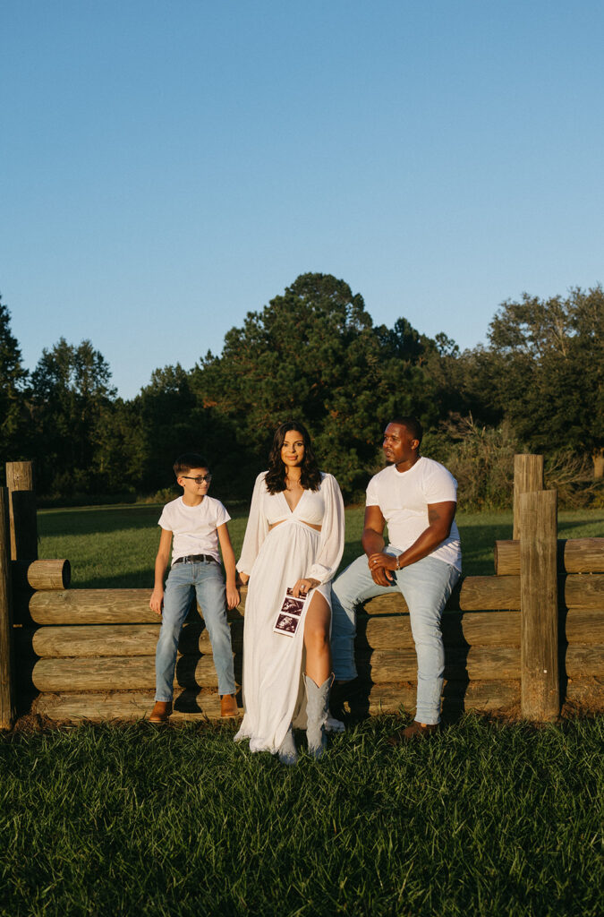 Jacksonville, Fl family announcing a pregnancy by sitting on wooden logs, holding an ultrasound picture